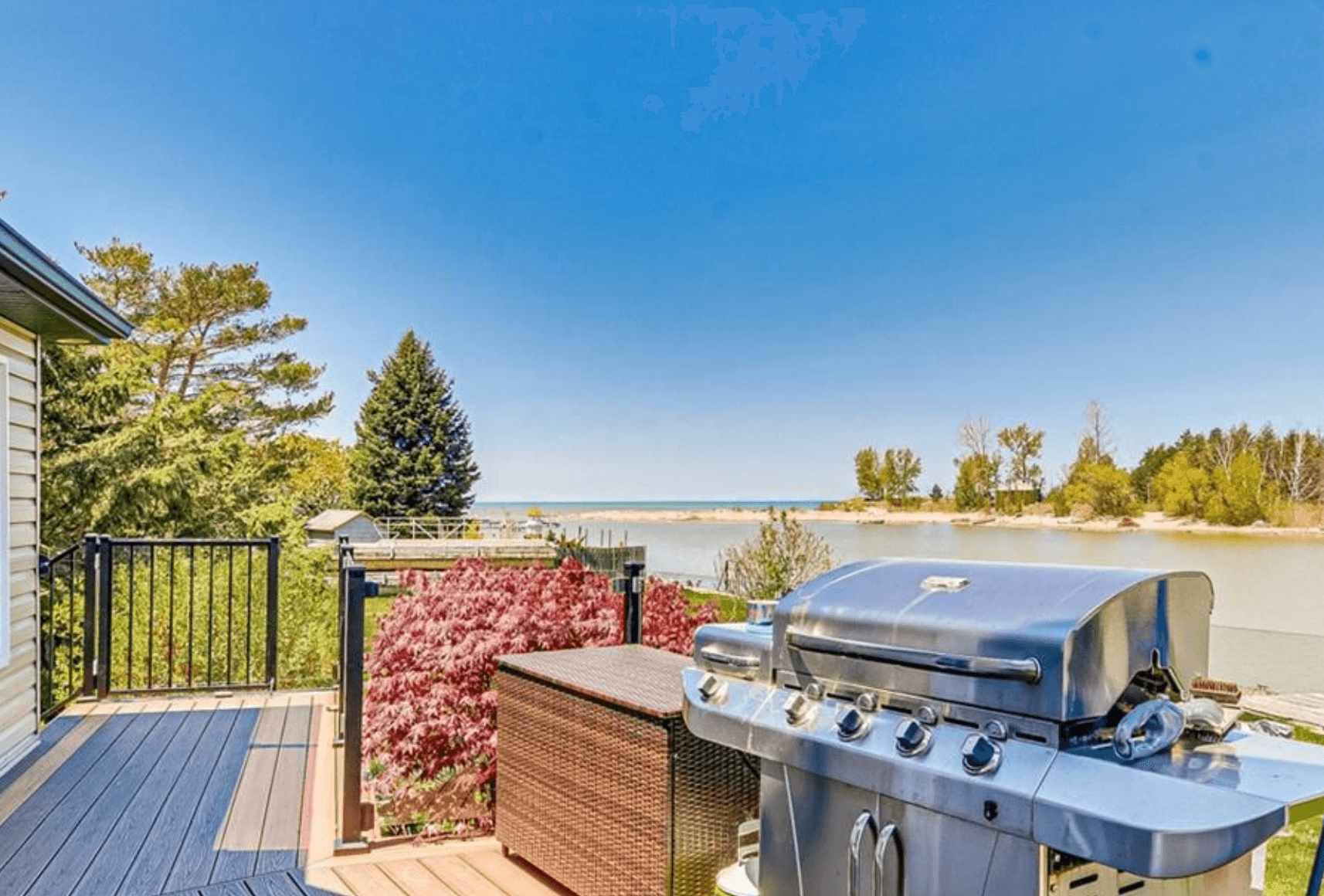 Stainless steel grill on a wooden deck overlooking a calm lake under clear blue skies.