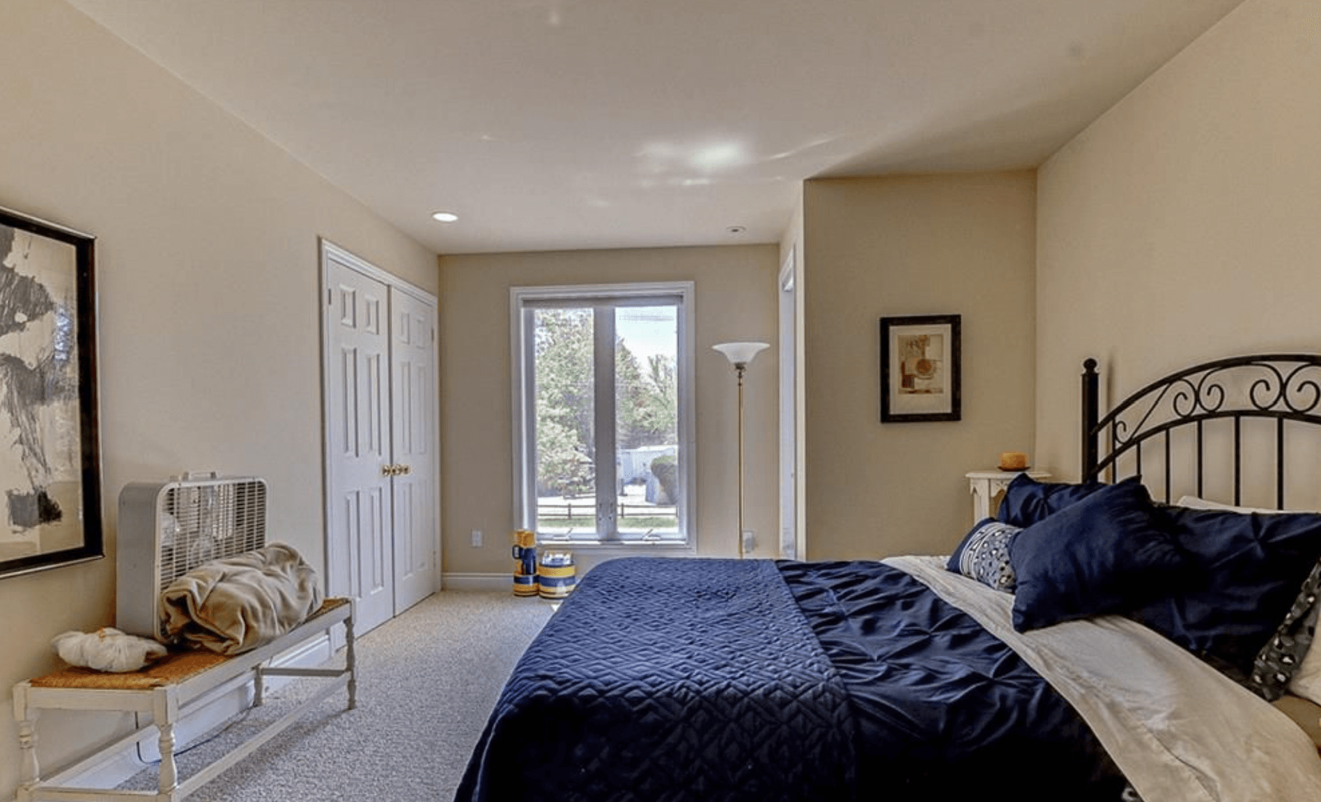 Neutral bedroom featuring a navy blue bed, wrought iron headboard, and large central window.