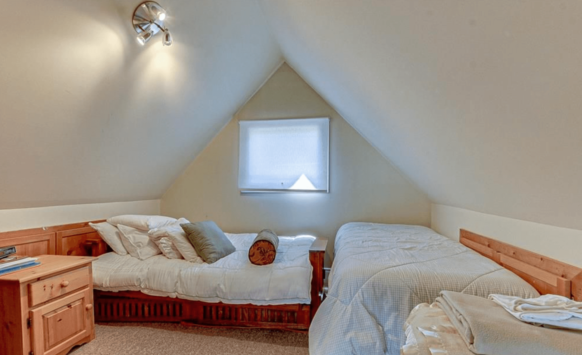 Attic bedroom with two twin beds, sloped ceilings, a wooden dresser, and a small window.