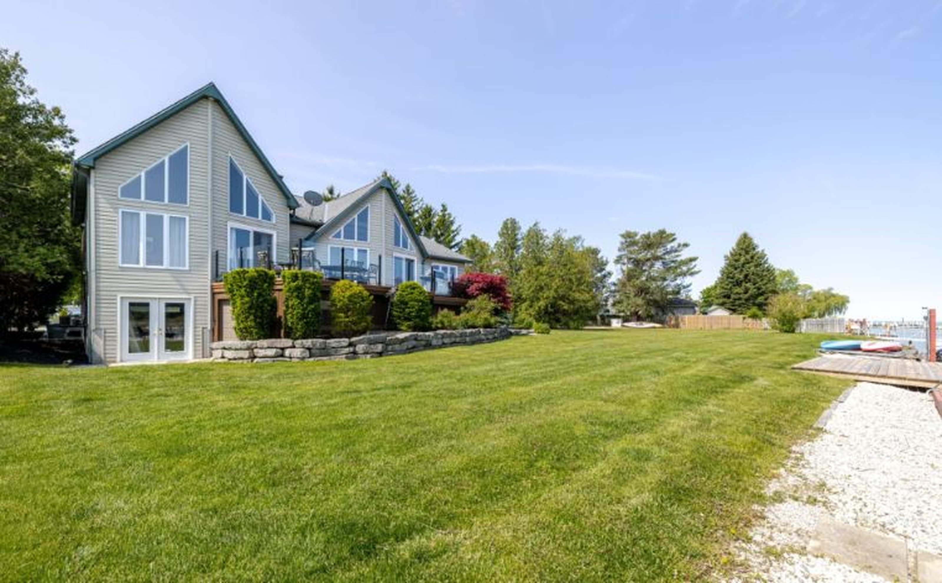 Modern grey house with large windows overlooking a vast green lawn near the water.