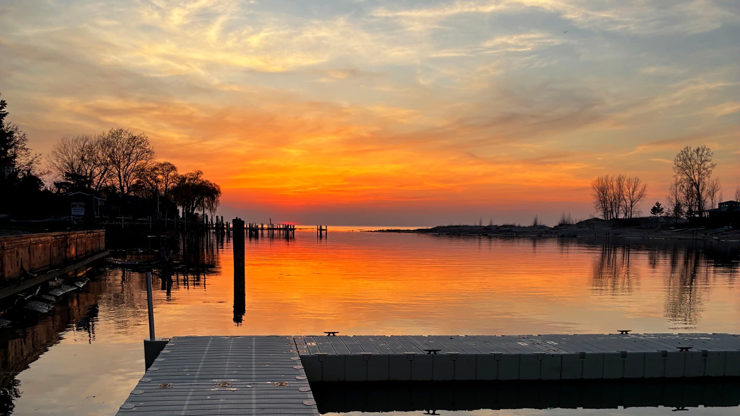 Vibrant orange sunset over calm water with a gray floating dock in the foreground.