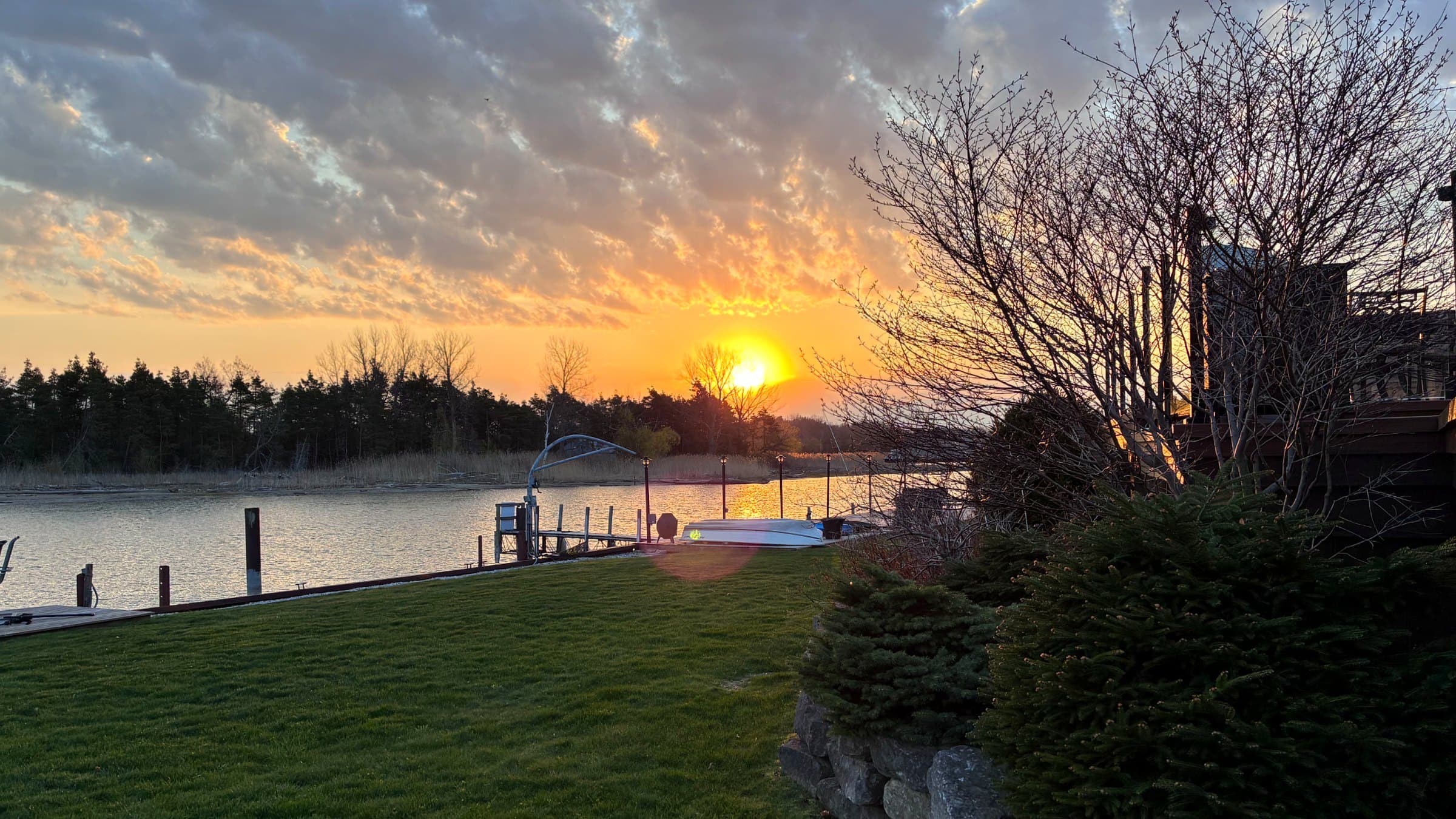 Vibrant orange sunset over a river with a boat dock, lawn, and silhouetted trees.