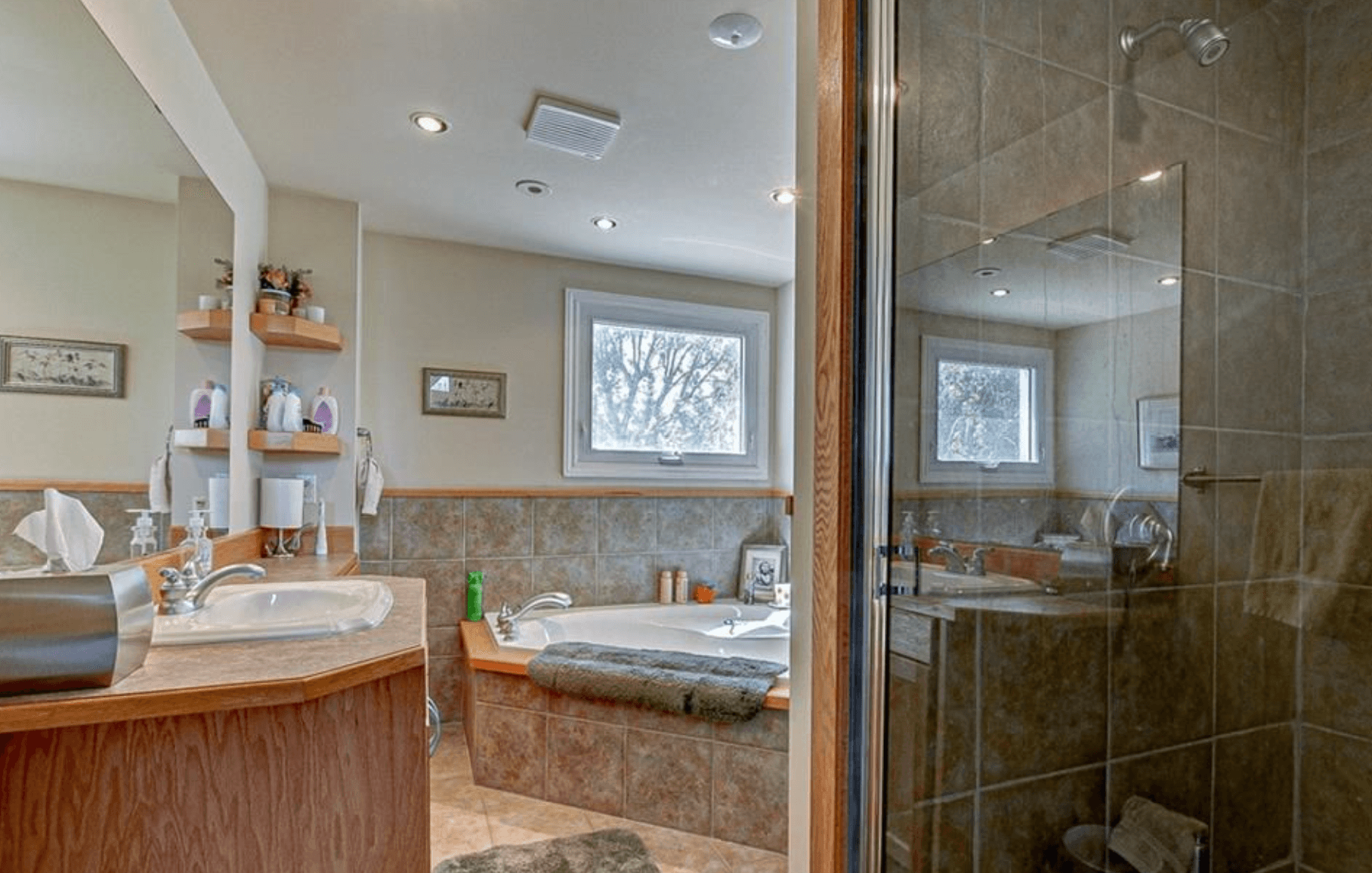 Modern bathroom featuring a wooden vanity, corner bathtub, and a glass-enclosed tan tiled shower.