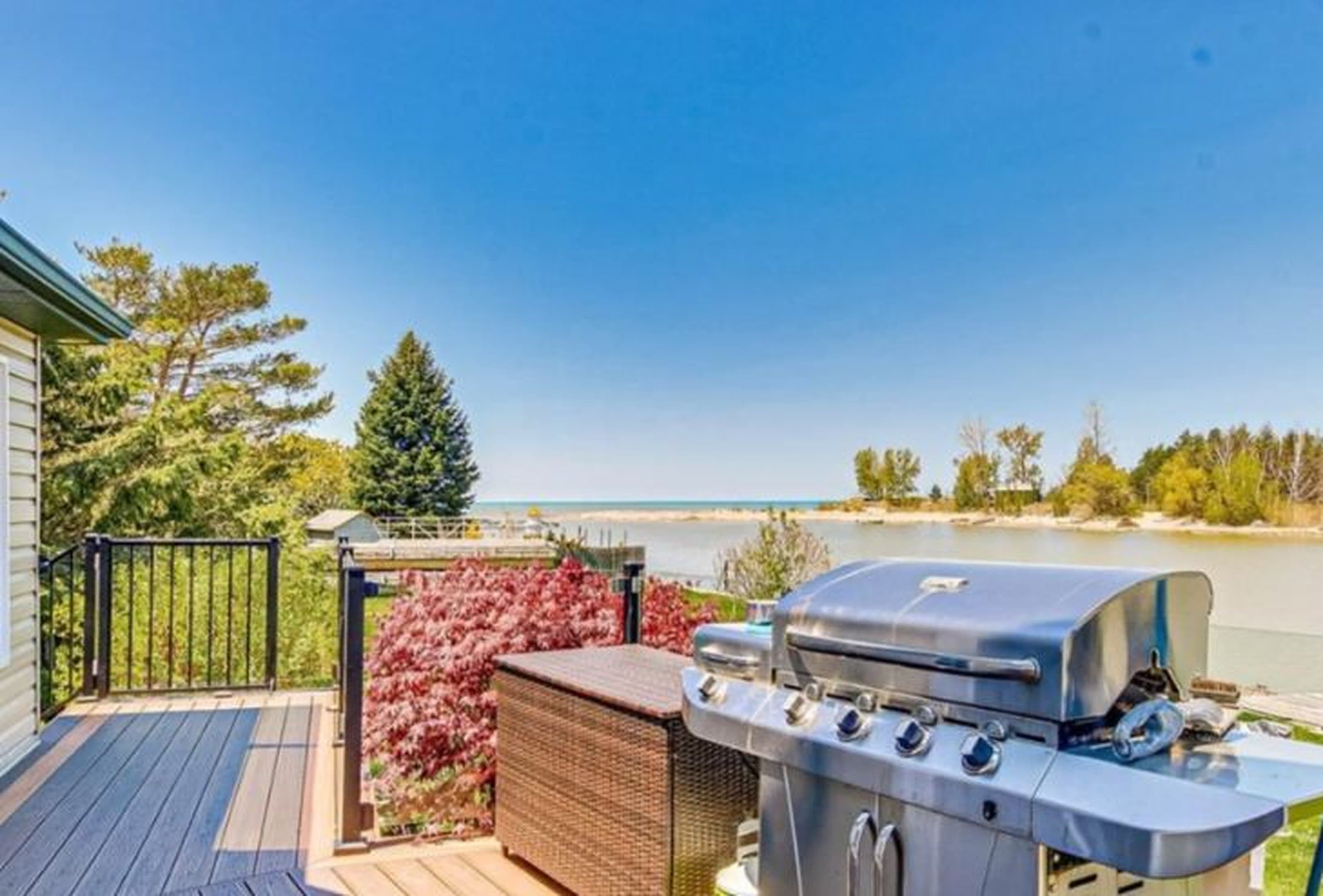 Stainless steel grill on a wooden deck overlooking a calm lake and clear blue sky.