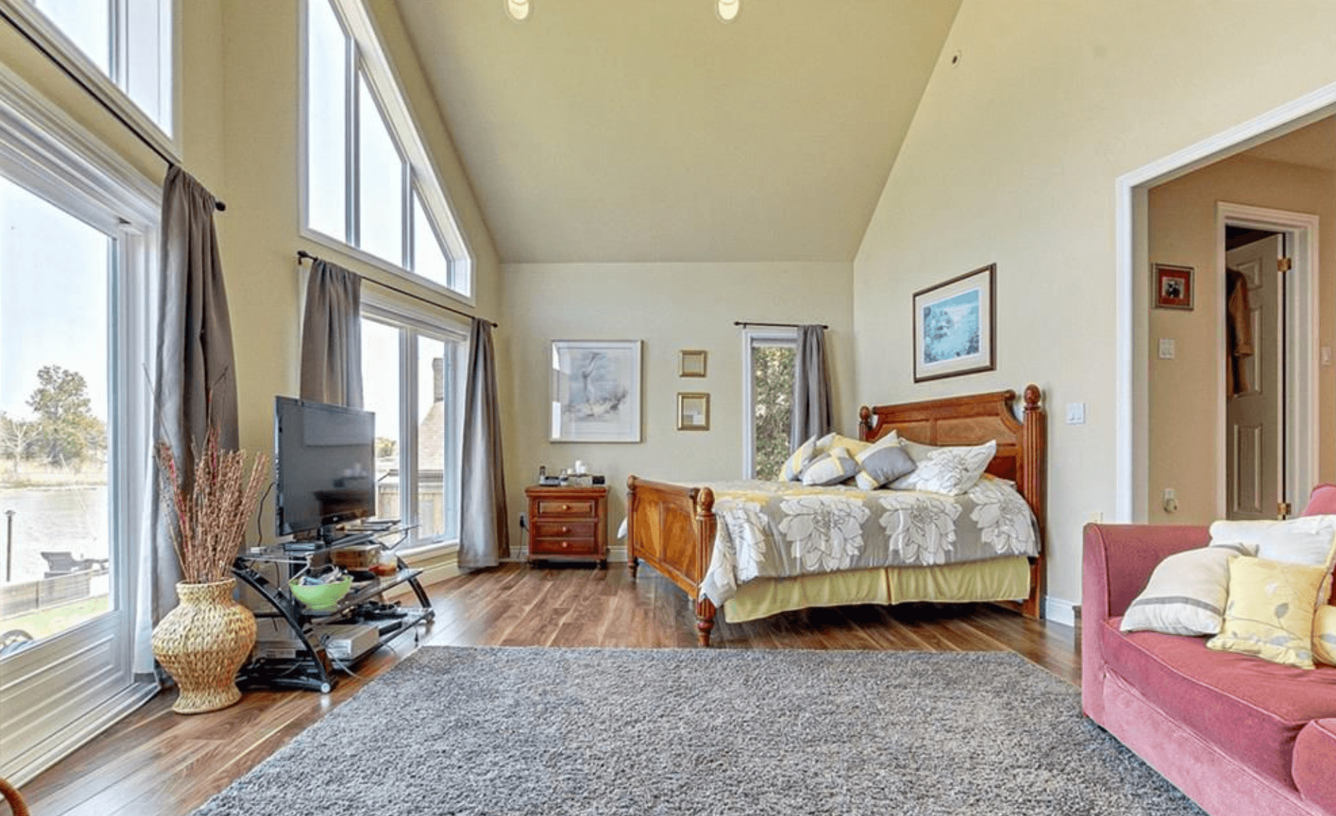 Spacious bedroom with vaulted ceilings, wooden bed, large windows, and a pink sofa.