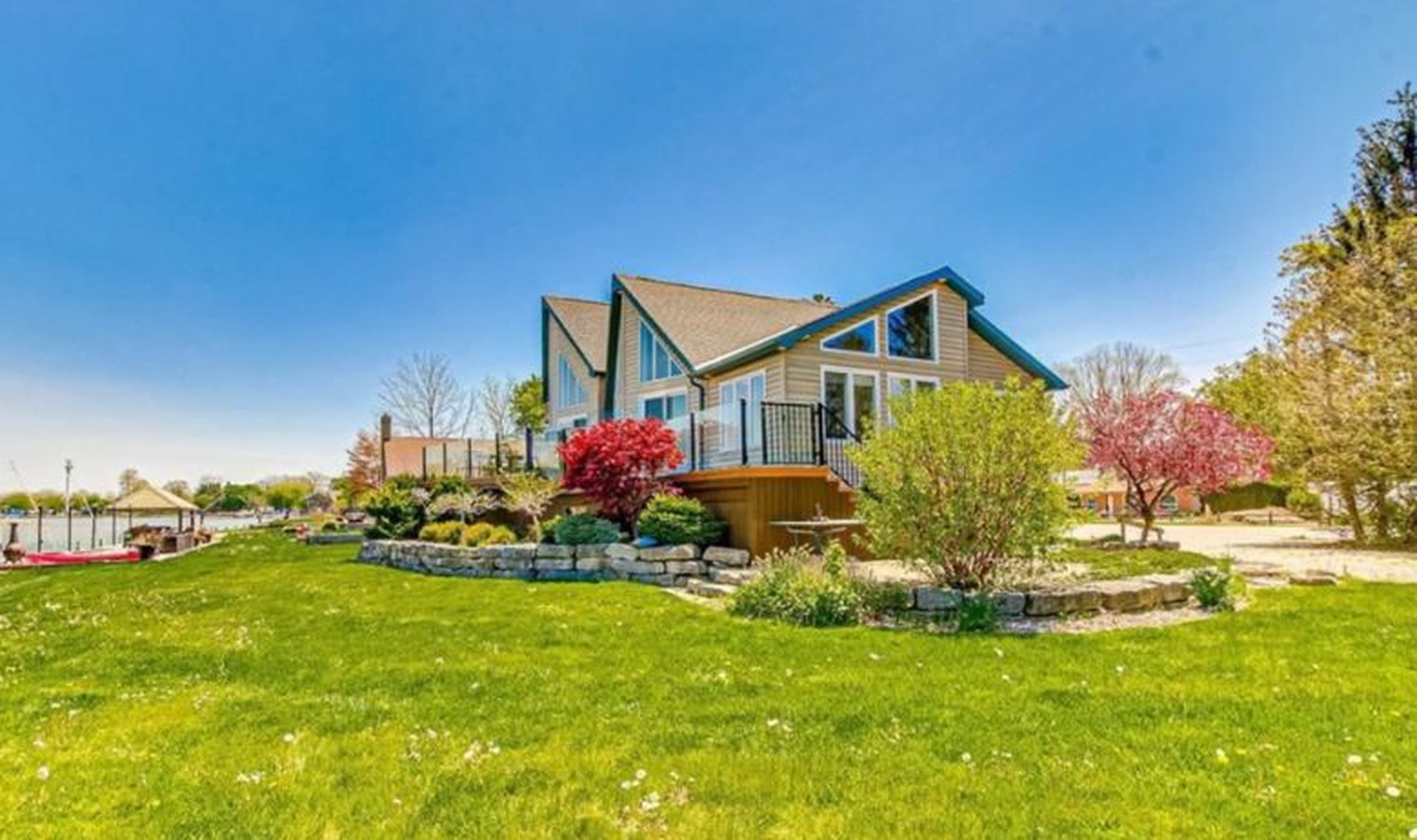 Modern tan house with large windows and deck overlooking a lush lawn and scenic waterfront.